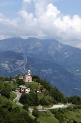 Green and blue mountain landscape with a small red church in Guardia, Trentino, Italy