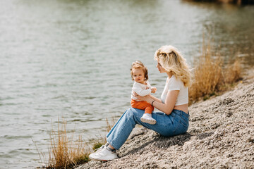 Young mother playing with her daughter outdoors, sitting by the lake.