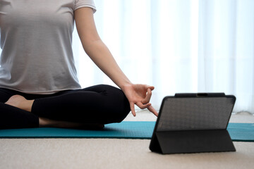 Naklejka premium The young lady is meditating on a mat with a tablet placed