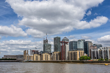 Obraz premium A mesmerizing view of a calm Thames river with beautiful buildings under a cloudy sky at Canary Wharf.