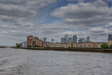 Naklejka premium A mesmerizing view of a calm Thames river with beautiful buildings under a cloudy sky at Canary Wharf.