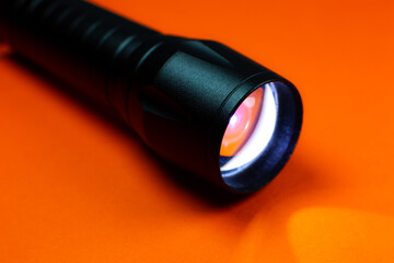 Black Flashlight and a ray of light on the orange background. Close up photo.