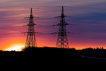Electricity poles at sunset. High voltage grid towers with wire cable at distribution station.