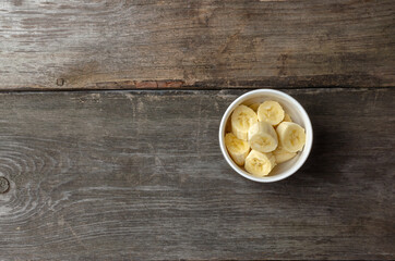 Fototapeta na wymiar Slices of bananas in a white plate on a rustic wooden background preparing for cooking with copy space.