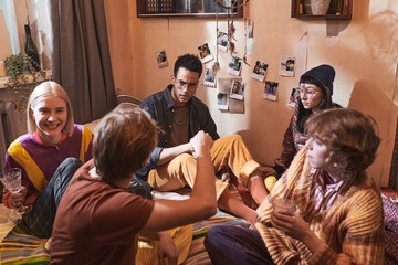 Group of friends sitting on the floor drinking alcohol drinks and talking to each other during domestic party at home