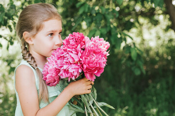 Obraz na płótnie Canvas portrait of a happy cute little caucasian seven year old kid girl, holds in hands and smell and enjoying a bouquet of pink peony flowers in full bloom on the background of nature
