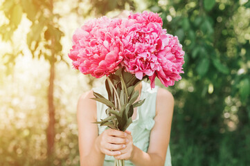 faceless little girl holds in hands a bouquet of pink peony flowers in full bloom on the background...