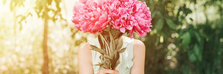 faceless little girl holds in hands a bouquet of pink peony flowers in full bloom on the background of nature. banner. flare