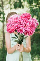 faceless little girl holds in hands a bouquet of pink peony flowers in full bloom on the background of nature