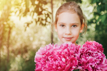 Naklejka premium portrait of a happy cute little caucasian seven year old kid girl, holds in hands a bouquet of pink peony flowers in full bloom on the green background of nature. flare