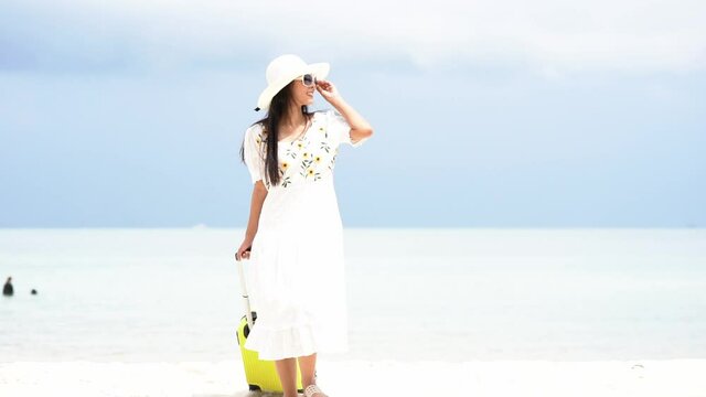 Summer vacations. Lifestyle woman relax and chill on beach.  Asian happy young people walking slow wearing white dress fashion and holding suitcase  in summer trips enjoy  tropical beach