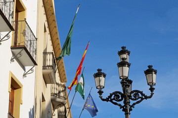 Fototapeta na wymiar Historic black metal lamp next to the flags of the town hall with blue sky in Vélez-Malaga, Spain, Europe 