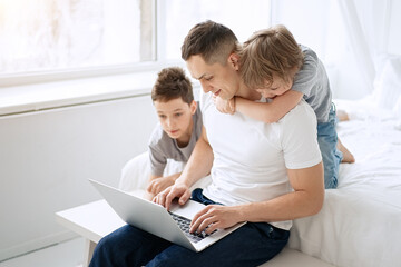 Fototapeta premium Work from home. Father working with children and laptop computer at home. Quarantine and closed school during coronavirus outbreak. 