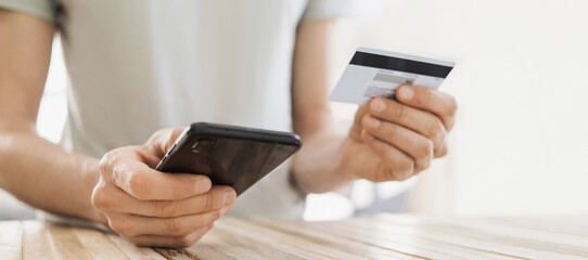 Man holding credit card and using smartphone at home, banner. Businessman shopping online, e-commerce, internet banking, spending money, working from home concept