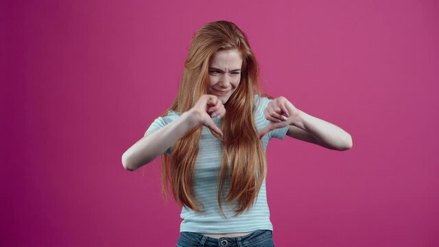 The red-haired, surprised girl rejects the information and depreciates it by gesturing, in a blue casual T-shirt, isolated on a pink background. The concept of people's lifestyle