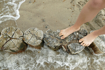 Summer feelings: A pair of naked feet standing on the wooden piles of a spur dike on the water's edge in the sea