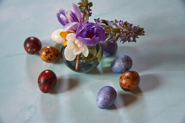A small vase with spring flowers and painted quail Easter eggs .