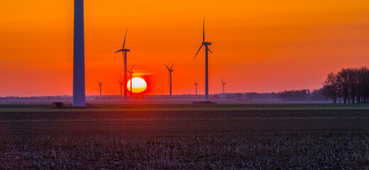 Wind turbines for renewable energy in an agricultural field in bright orange yellow sunlight at sunrise in spring, Almere, Flevoland, The Netherlands, April 17, 2021