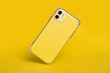 Yellow iPhone 11 in clear silicone case falls down isolated on yellow background back view. Phone...