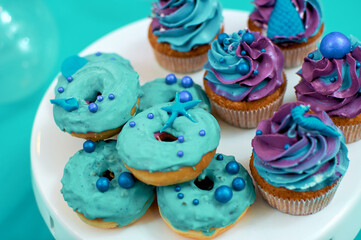 Cream muffins and mini donuts. Baking for a children's party with a marine theme. Desserts in blue.