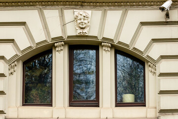 Art Nouveau arch window, decoration and surveillance camera. Detail of old building facade. Cracked decoration of child up of exterior arched window at Art Nouveau building in Riga, Latvia, Europe 