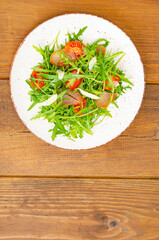 Dish of arugula, tomatoes, dried meat and cheese. Salad on plate on wooden background