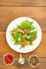 Dish of arugula, tomatoes, dried meat and cheese. Salad on plate on wooden background