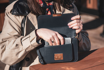 A woman in a light raincoat puts her phone in her purse.