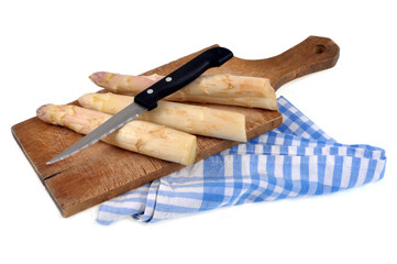 Asperges crues avec un couteau sur une planche à découper posée sur un torchon à carreaux en gros plan sur fond blanc