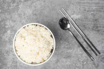 Top view steamed rice in a stainless bowl with spoon and chopsticks on the gray concrete table