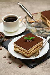 Portion of Traditional Italian Tiramisu dessert and mocha coffee maker on grey concrete background