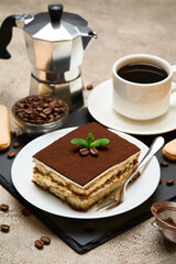 Portion of Traditional Italian Tiramisu dessert and mocha coffee maker on grey concrete background