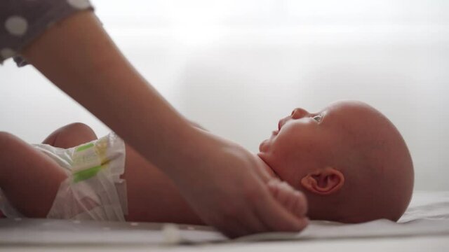 Mother with baby boy doing exercise simple exercises to make baby bones and muscles stronger, newborn infant lying on bed against the window. High quality 4k footage