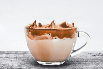 Big glass cup fluffy coffee with milk or сreamy caramel whipped latte on cold gray background wooden table. Close