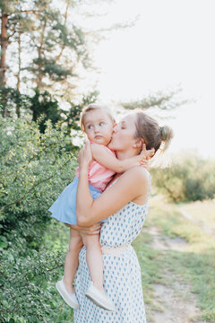 young mother of European appearance 20-25 years spends time with her daughter 1-3 years. bright image, calm tones. warm picture. summer day. family on a background of pine forest. clothes in light 