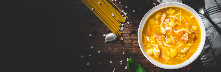 Chicken soup with noodles and vegetables in white bowl on wooden table background