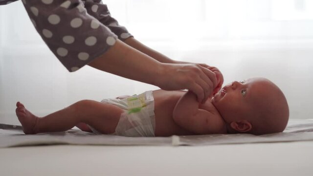 Mother with baby boy doing exercise simple exercises to make baby bones and muscles stronger, newborn infant lying on bed against the window. High quality 4k footage