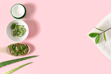Top view of wooden spoon with aloe vera juice, organic cream, gel, towel and green leaves. Flat lay composition with aloe vera slices on pink background. Copy Space for text. Natural cosmetics concept