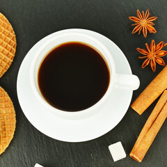 A cup of aromatic coffee, waffles, cinnamon and sweets on a black.