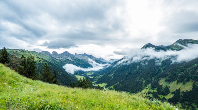 Praderas verdes, bosques de con&iacute;feras, nubes bajas y altas de lluvia penetrando por un valle lateral del gran valle de Ar&aacute;n, en los Pirineos espa&ntilde;oles