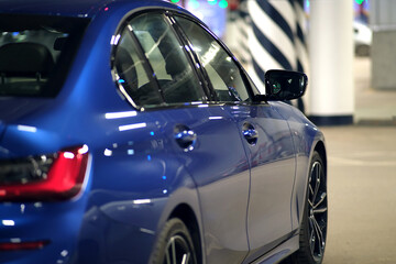 Close-up of the left side mirror with the turn signal repeater and the window of the body of a blue sedan in the street parking lot after washing and detailing at the service station. 