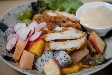 Fried chicken salad, creamy salad dressing, fruit and vegetables, reddish cantaloupe on a light brown background.