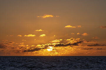 Warm and romantic sunset on the North Sea with small clouds hiding half of the sun