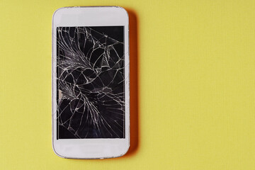 Broken mobile phone with cracked display on yellow background.