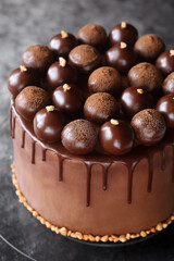 Contemporary Chocolate Truffle Layer Cake with chocolate smudge, decorated with handmade chocolate truffles, on a dark gray background.