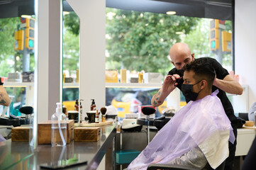 Barber cutting man hair with scissors wearing mask
