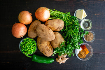 Samosa Potatoes Ingredients on a Dark Wood Background: Raw potatoes, onions, peas, herbs, and...