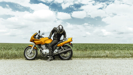 The biker sits on a yellow motorcycle and looks back, the motorcycle has broken down