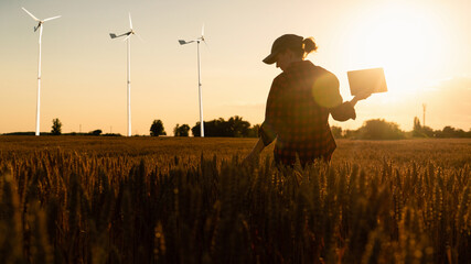 Farmer in a wheat field. Wind turbines in the field. Clean energy.