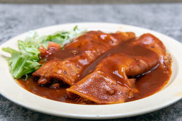 Chicken enchiladas smothered in tasty red sauce on a plate makes for a filling and hearty entree.
